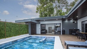 A modern outdoor pool area with a built-in hot tub, seating, and a covered patio.