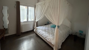 Ein Schlafzimmer mit einem Himmelbett, einem Fenster mit Vorhängen, einem Heizkörper und einem Nachttisch mit Lampe.