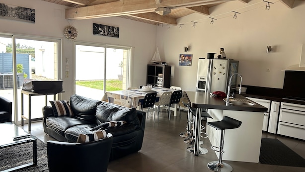 Eine moderne Küche mit Kochinsel, ein Essbereich mit Tisch und Stühlen, ein Wohnzimmer mit Ledersofa und eine große Schiebeglasdoor zum Patio.