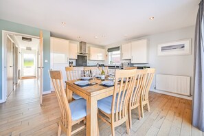 A modern kitchen with wooden cabinets, a dining table set for four, and a view of the outdoors.
