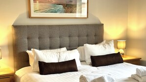 A neatly made bed with white and brown pillows, a headboard, and a framed picture above.