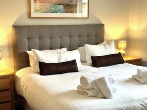 A neatly made bed with white and brown pillows, a headboard, and a framed picture above.