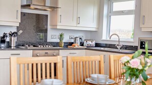 A modern kitchen with granite countertops, stainless steel appliances, and wooden chairs.