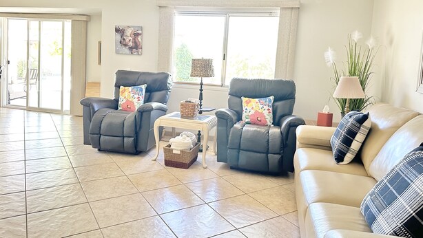 A spacious living room with two leather armchairs, a beige sofa, a small coffee table, and a large window providing natural light. - Spacious Vacation Home Sun City West 55 Community (Sun City West)
