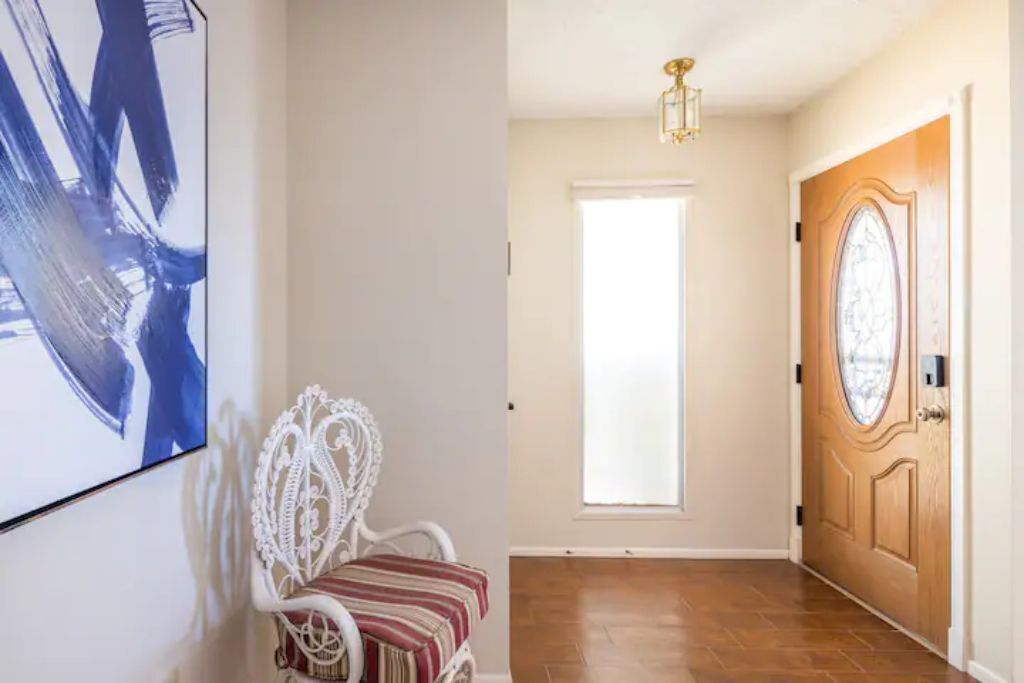 A hallway with a white chair, a wooden door, and a large window.