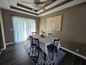 A dining area with a table, chairs, a ceiling fan, a window with curtains, and a painting on the wall. - Willit. 4BR Home w/ large backyard. (Omaha)