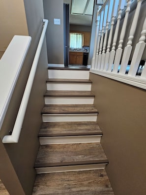 A staircase with wooden steps and white railings leading to a kitchen area. - Willit. 4BR Home w/ large backyard. (Omaha)