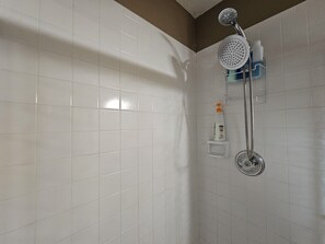 A bathroom with white tiled walls, a shower with a handheld showerhead, and a bottle of shampoo on a shelf. - Willit. 4BR Home w/ large backyard. (Omaha)