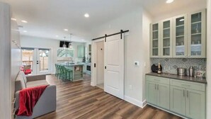 Una cucina moderna con pensili verde chiaro, un'area pranzo con sedie verdi e un pavimento in legno.