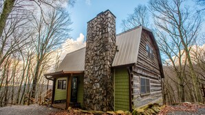 Eine Blockhütte mit einem Steinkamin, einer Veranda und Blick auf den umliegenden Wald.