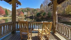Eine Holzterrasse mit zwei Holzstühlen, die auf einen ruhigen See mit Herbstlaub blicken.