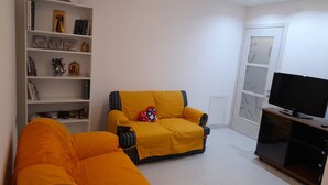 A living room with a sofa, a television, and a bookshelf. - Comfortable apartment just minutes from the city (Su Planu)