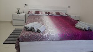 A neatly made bed with a patterned bedspread, two pillows, and rolled towels on a white nightstand. - Comfortable apartment just minutes from the city (Su Planu)