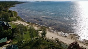 Een kustpand met een zandstrand, een klein steiger en een huis met een groen dak.