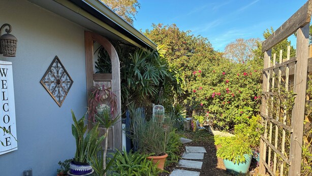 A garden pathway leading to a house with a welcome sign, potted plants, and a wooden fence. - Sarasota Cozy & Clean, Near #1 Beach Siesta in SouthGate Neighborhood  (Sarasota)