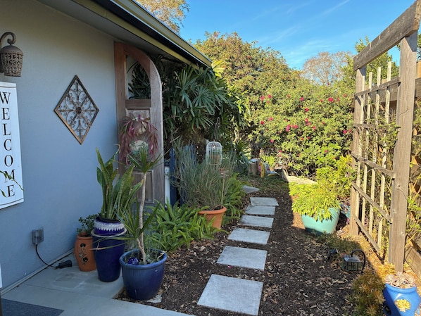 A garden pathway leading to a house with a welcome sign, potted plants, and a wooden fence.
