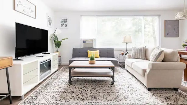 A modern living room with a flat-screen TV, a grey sofa, a beige sofa, a coffee table, and a patterned rug. - King & Queen Luxury Memory Foam Beds near Cleveland Airport | Georgetown Villas (Fairview Park)