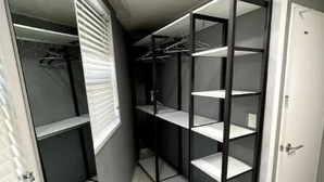 Un dressing avec de nombreuses étagères et un espace pour suspendre les vêtements, une porte dotée d’une poignée et un sol carrelé.