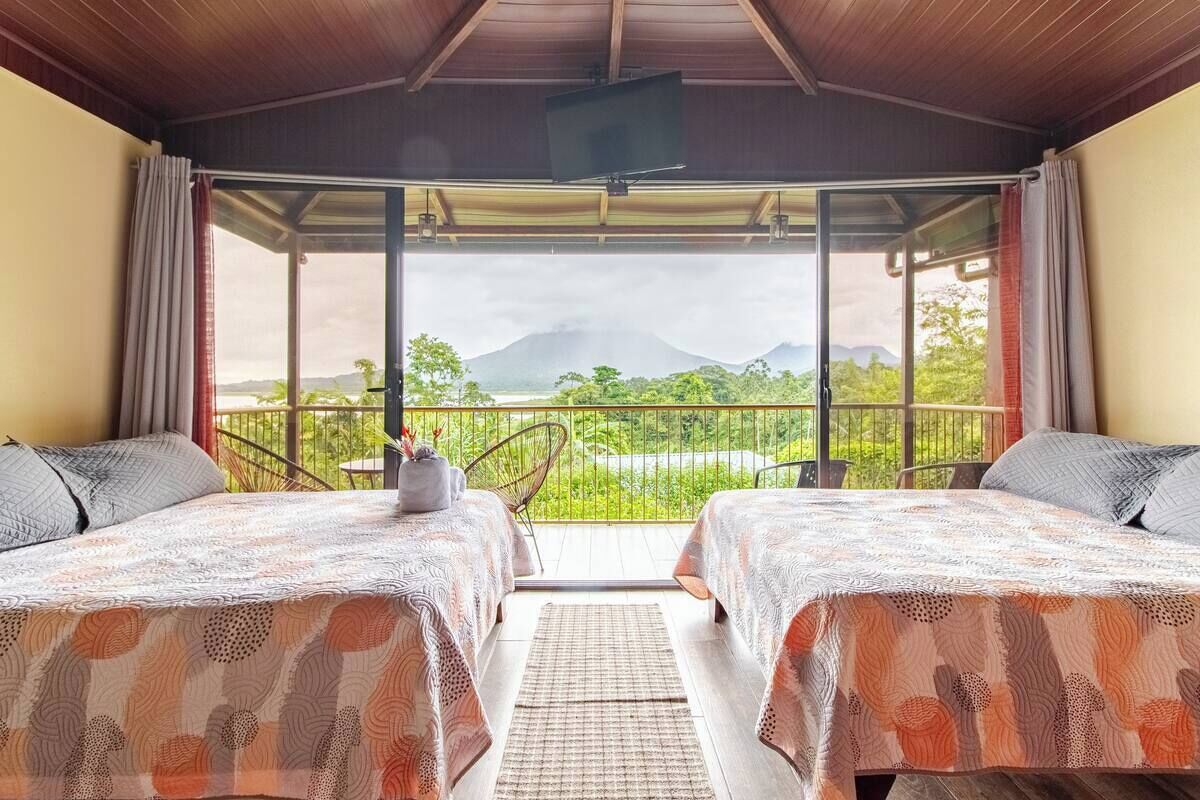 A room with two beds, a TV, and a balcony with a view of mountains.