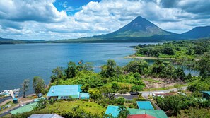 A coastal village with a prominent volcano in the background, surrounded by lush greenery and a calm sea. - Villas Paradise (La Fortuna)
