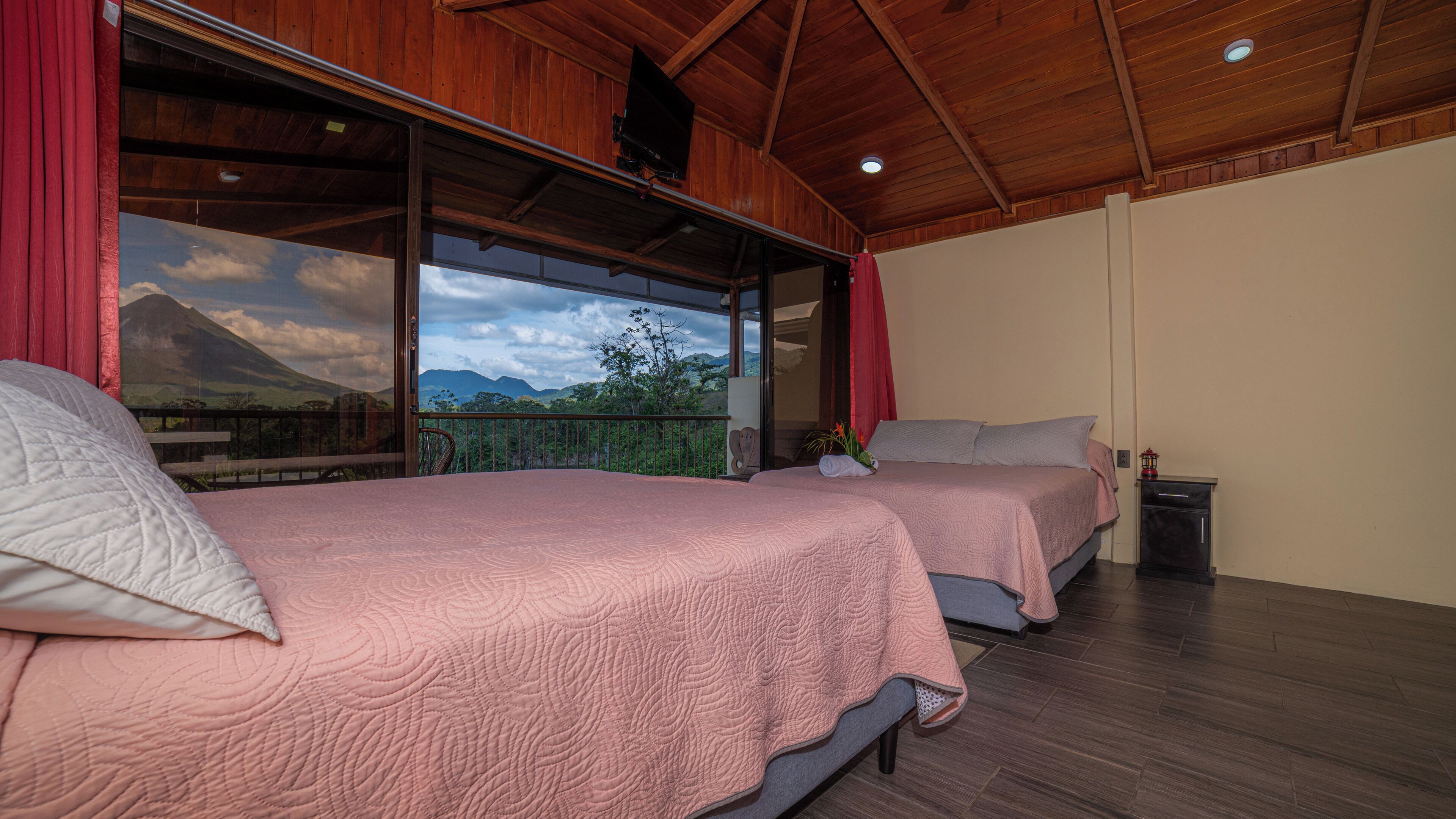 A bedroom with two beds, wooden flooring, and a large window offering a mountain view.