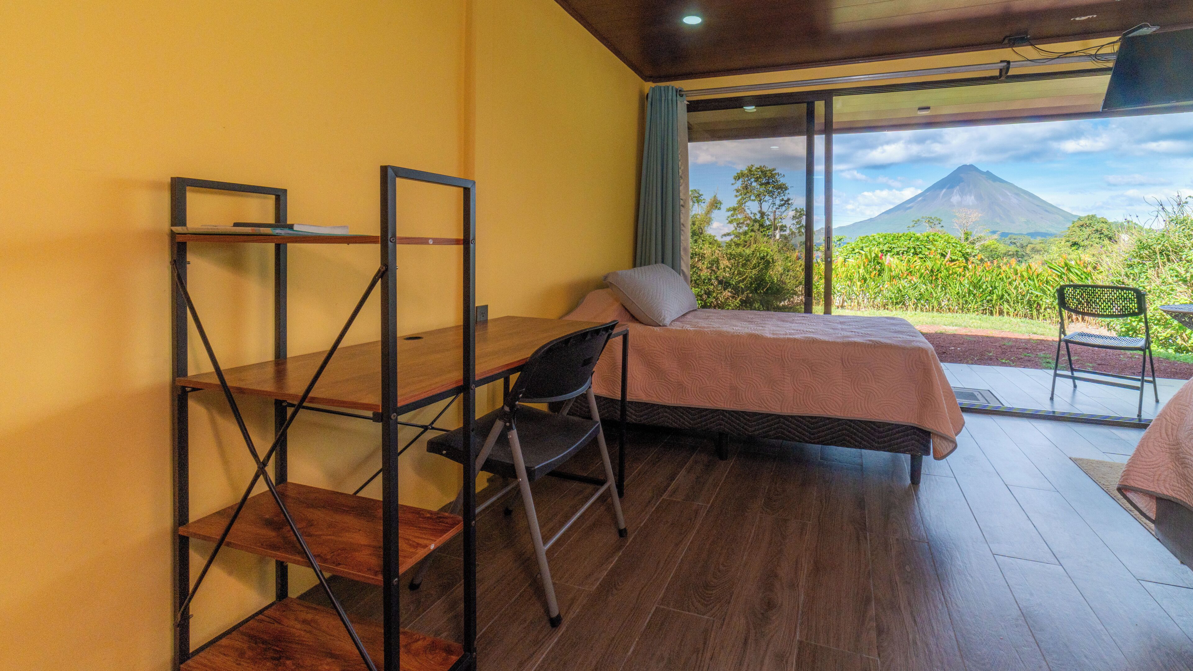 Een slaapkamer met een bed, een bureau en een stoel, met uitzicht op een berg en groen.