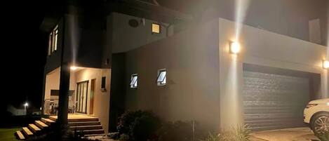 A modern house at night with a driveway and steps leading to the entrance.