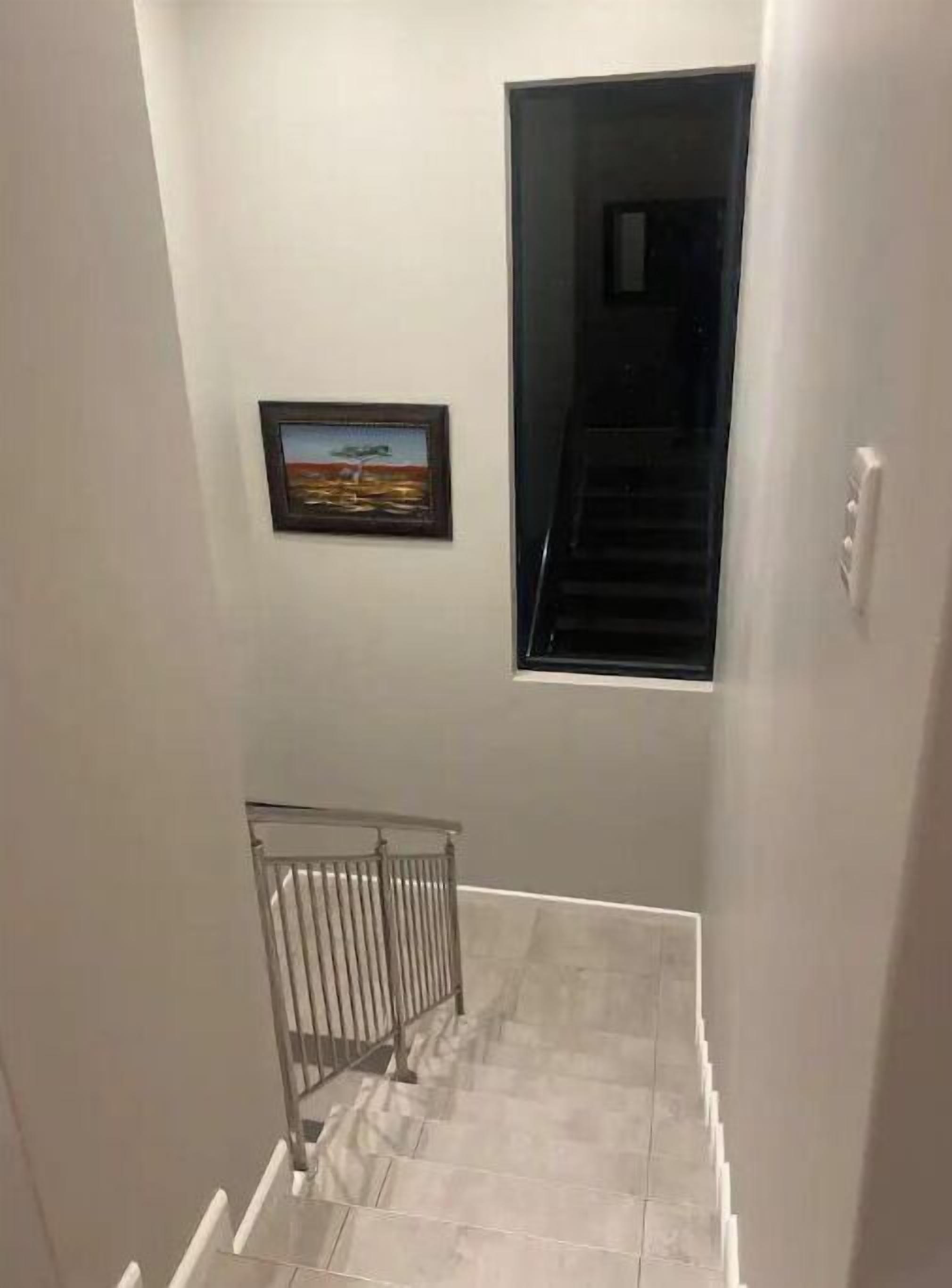 A narrow stairway with a metal railing, a framed picture on the wall, and a window at the top.