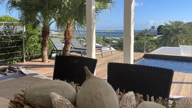 Ein überdachter Außenbereich mit Liegestühlen, einem Pool und Blick auf das Meer.