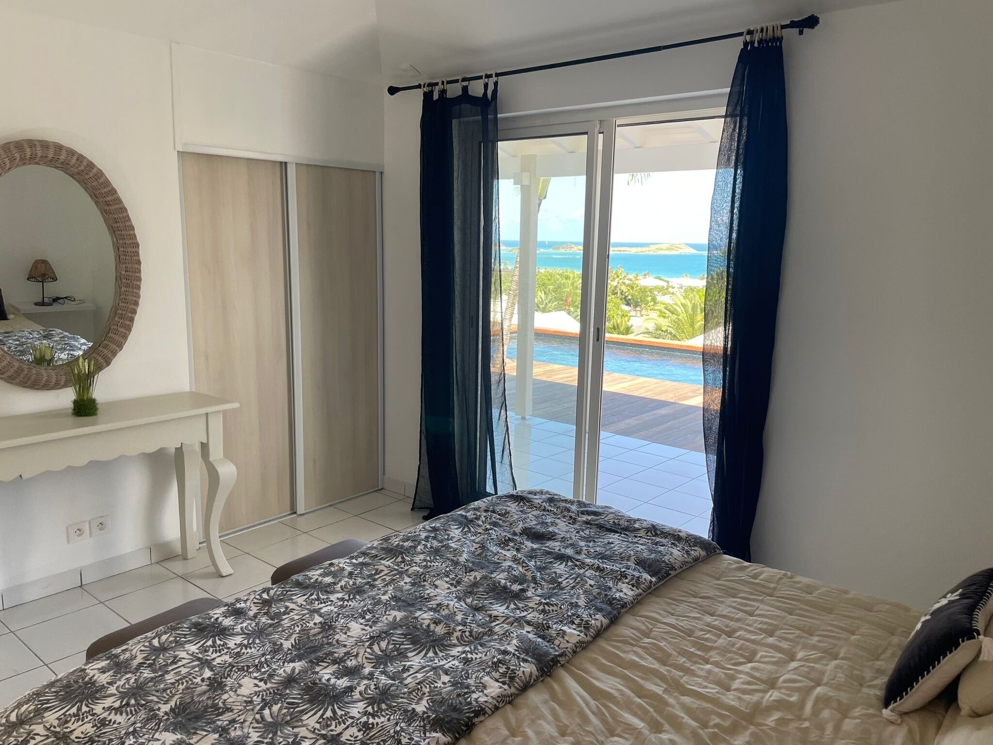 A bedroom with a bed, a dresser, a mirror, and a view of the ocean through a sliding glass door.