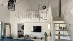 Ein großzügiges Wohnzimmer mit einem großen, blauen Sofa, einem flachbildfernseher an der Wand und einer weißen Treppe mit Geländer.