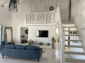 Relax in this spacious living area with a high ceiling, featuring a large flat-screen TV and comfortable seating.