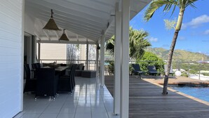 Ein überdachter Außenbereich mit Esstisch und Stühlen, einem Pool und Blick auf Berge.