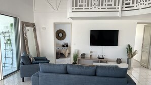 Ein modernes Wohnzimmer mit einer großen, grauen Couch, einem flachbildfernseher an der Wand und einem Holztischchen mit Dekoration.