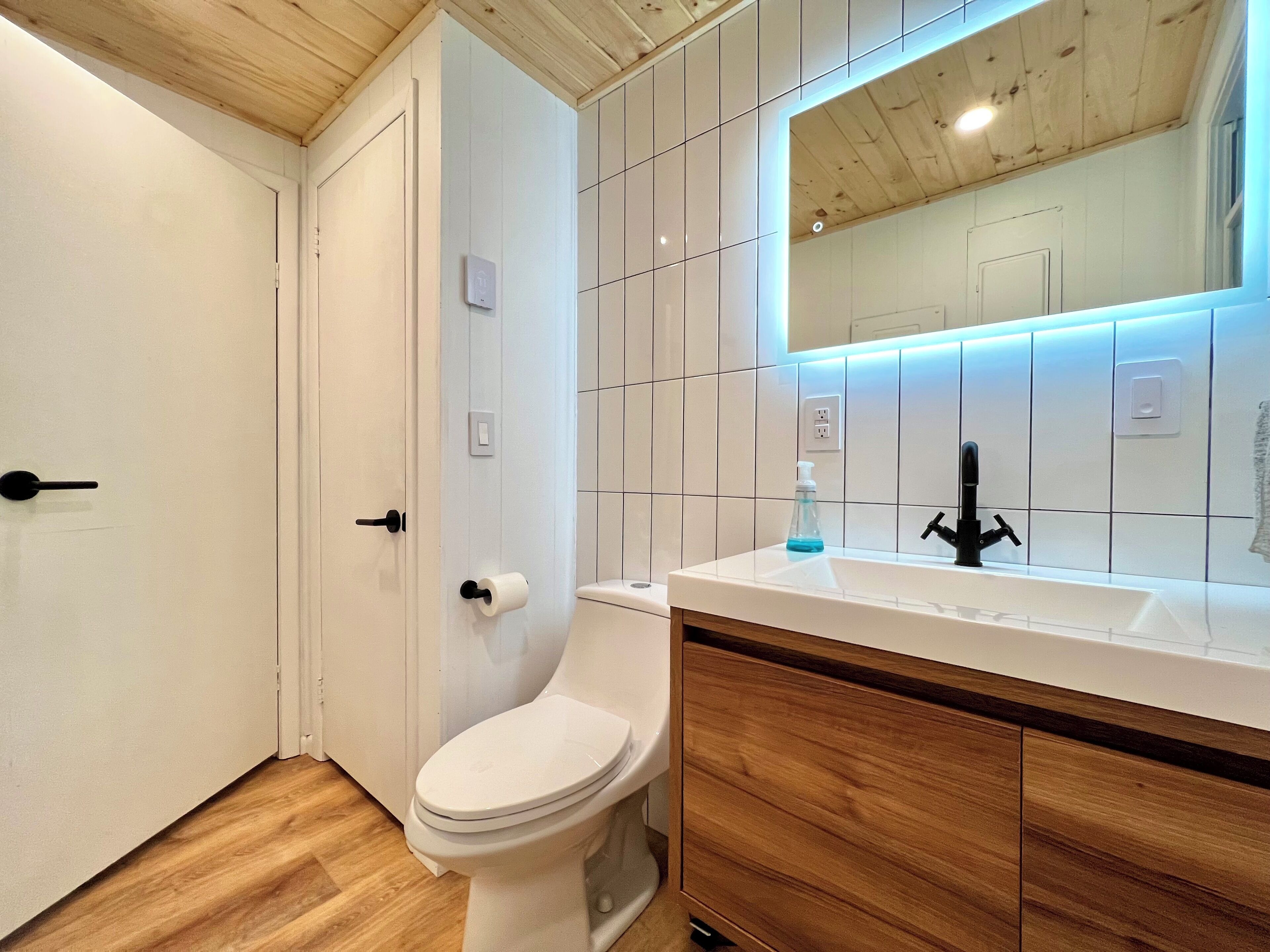 Une salle de bain moderne avec des toilettes blanches, des meubles en bois et un lavabo blanc doté d’un robinet noir.