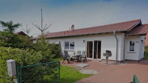 A single-story house with a red-tiled roof, a front door, and a small patio area with a table and chairs. - Vacation home in a quiet location, 200m from the nature reserve lake, Mönchshof 13a, with WLAN (Eldetal)