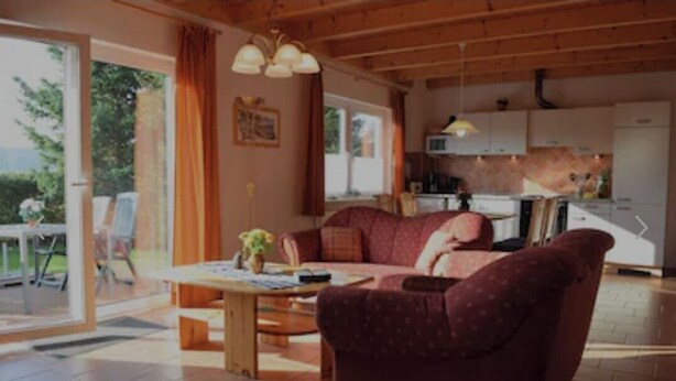 A cozy living room with a sofa, a coffee table, and a dining area with chairs. There is a kitchen in the background with cabinets and a microwave. - Vacation home in a quiet location, 200m from the nature reserve lake, Mönchshof 13a, with WLAN (Eldetal)