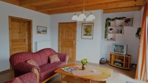A cozy living room with a red sofa, wooden coffee table, and a television on a wooden stand. - Vacation home in a quiet location, 200m from the nature reserve lake, Mönchshof 13a, with WLAN (Eldetal)