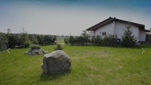 A white building with a sloped roof, surrounded by a well-maintained lawn and a row of trees. - Vacation home in a quiet location, 200m from the nature reserve lake, Mönchshof 13a, with WLAN (Eldetal)