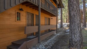A wooden cabin with a porch, stone steps, and a large tree nearby. - Cozy Cabin-Style Condo in Central Location (Mammoth Lakes)