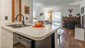 A modern kitchen with a dishwasher, a large island, and a fireplace. - Cozy Cabin-Style Condo in Central Location (Mammoth Lakes)