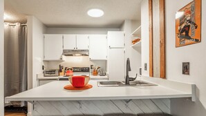 A modern kitchen with white cabinets, a central island with a sink, and a red kettle. - Cozy Cabin-Style Condo in Central Location (Mammoth Lakes)