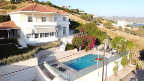 Un bâtiment blanc à deux étages, doté d’une piscine et entouré de verdure et de collines.