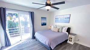 Une chambre à coucher avec un lit, un ventilateur de plafond, une fenêtre avec des rideaux, un tableau et une table de chevet.