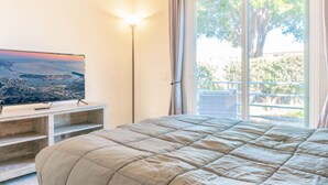 Une chambre avec un grand lit, un téléviseur posé sur un meuble en bois, et une vue sur le paysage urbain par la fenêtre.