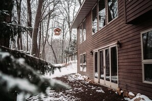 A wooden house with a snow-covered ground and a bird feeder hanging from a tree.