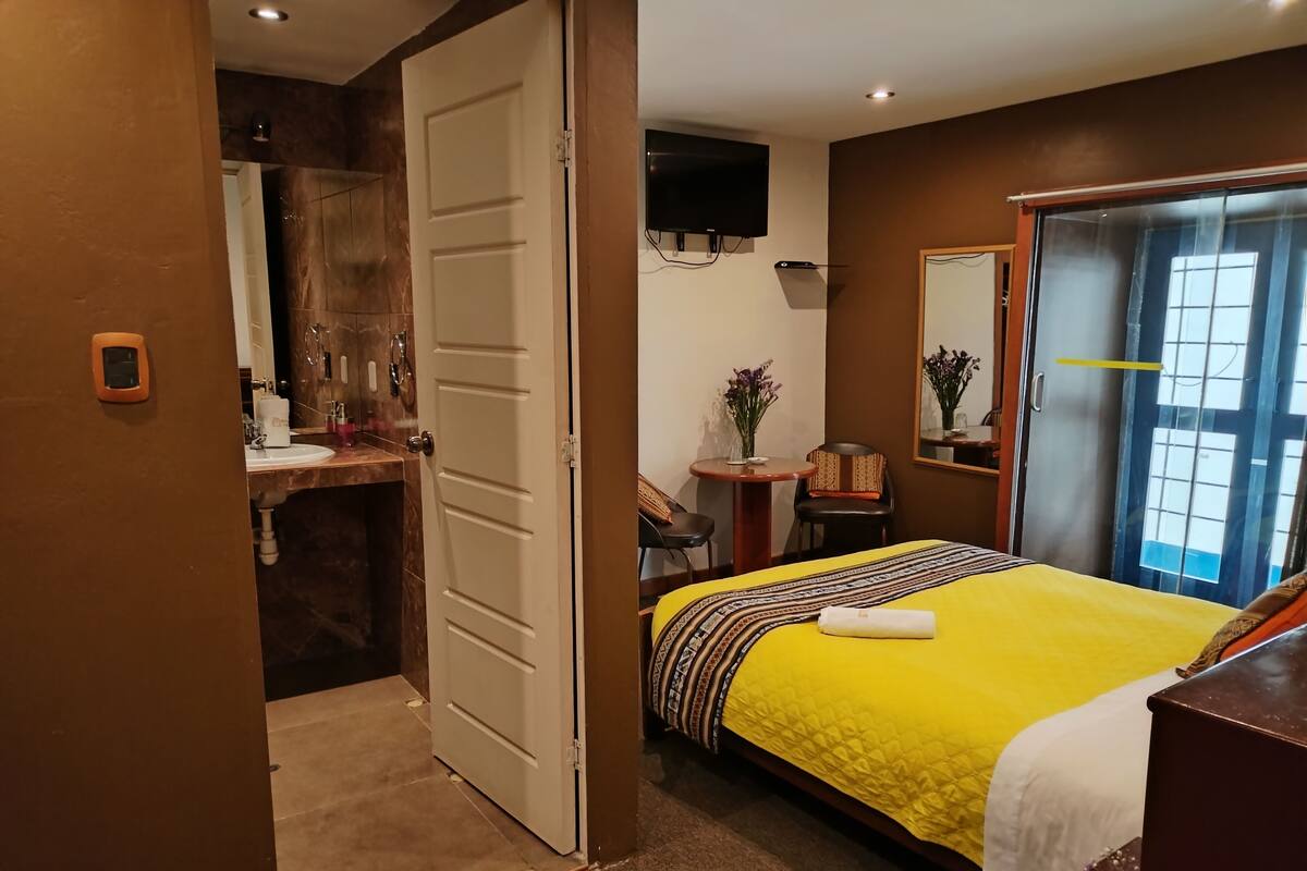 A hotel room with a bed, a desk, a TV, a bathroom, and a door.