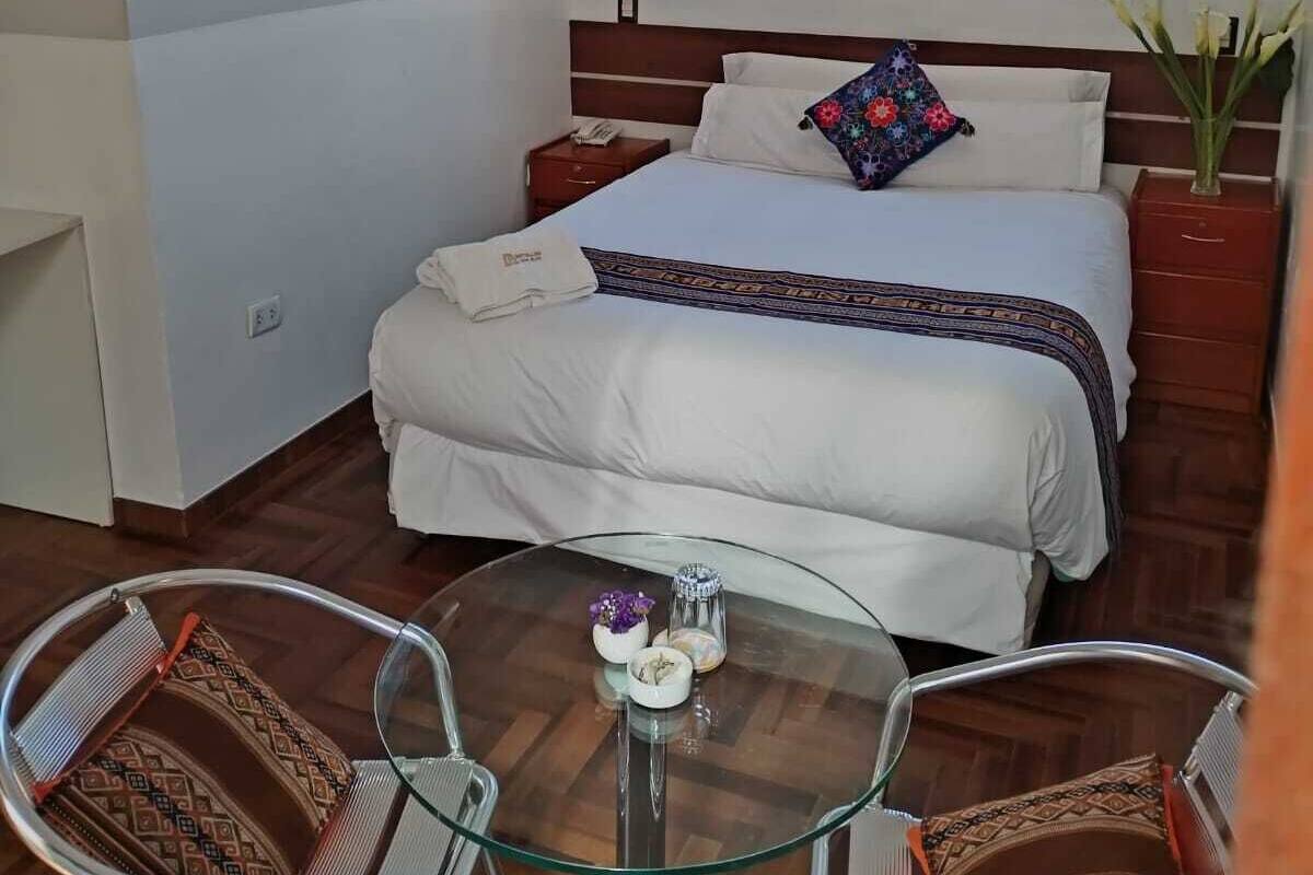 A hotel room with a bed, a desk, a chair, a glass table, and a window with curtains.