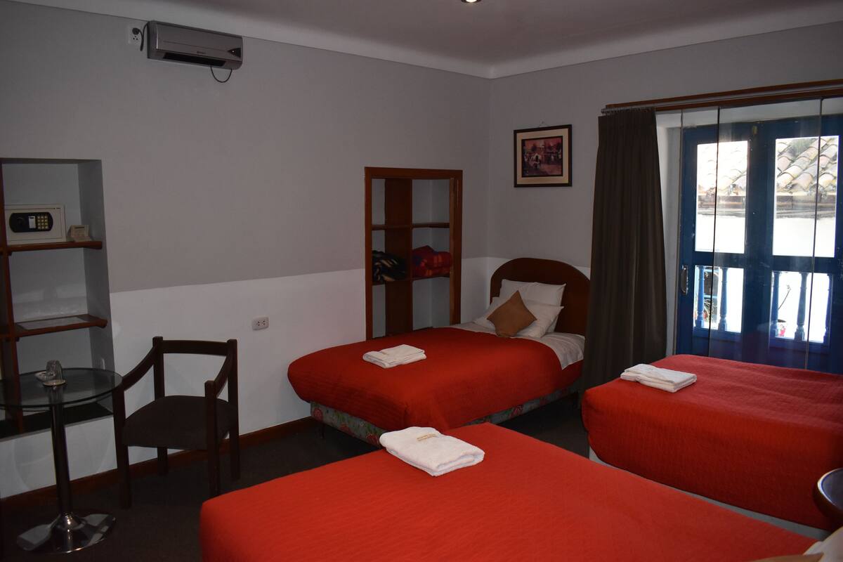 A hotel room with two beds, a desk, a chair, a shelf with a radio, and a window with curtains.