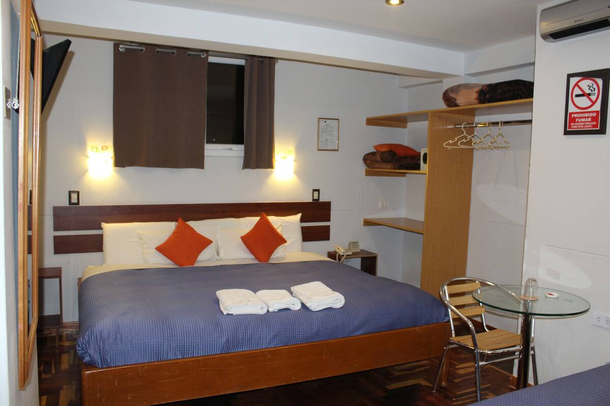 A hotel room with a bed, a bedside table, a chair, a small table, and a wardrobe.